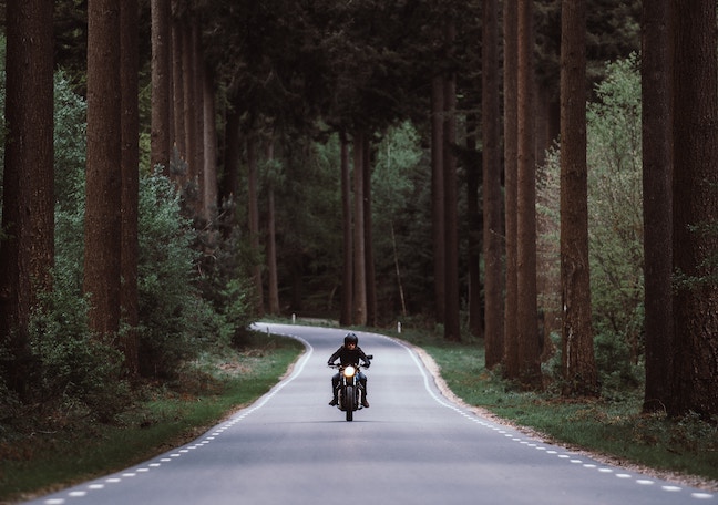guy on motorcycle on open road through the woods -unsplash